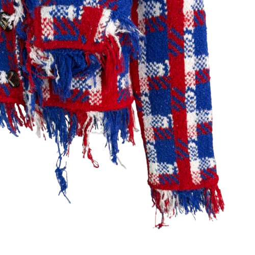 A close-up of a red, white, and blue plaid fringed knit textile, showing the pattern and tassels against a plain white background.
